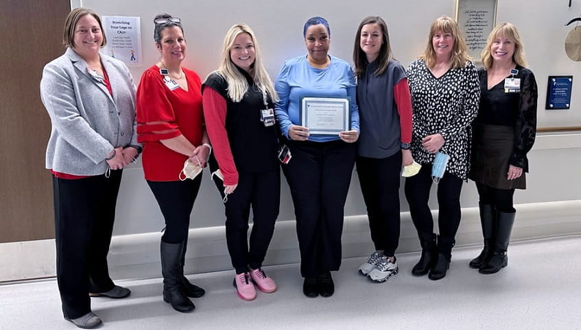 A group of seven women stand and smile at the camera. The one in the middle is Jackie Franklin, and she holds her award.
