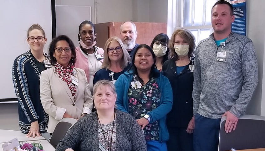 A diverse group of staff stands together and smiles for the camera. 