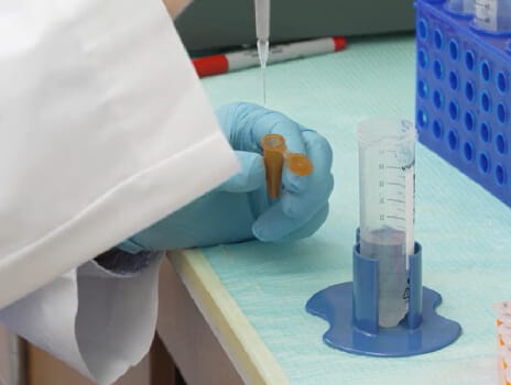 hands putting liquid from a needle into a test tube