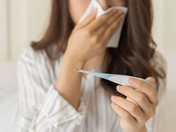 Woman blowing her nose and looking at a thermometer