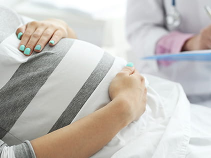 Pregnant mother holding her stomach while speaking to a doctor