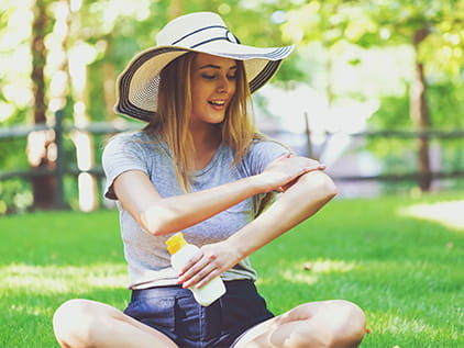 Girl in sun hat applying sunscreen.